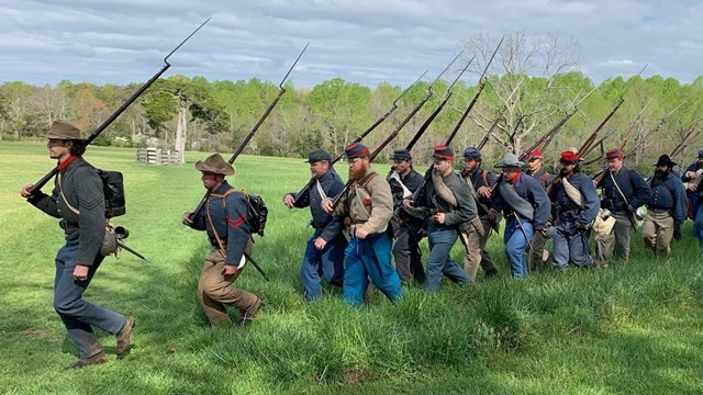Civil war era dressed soldiers march through a grassy field