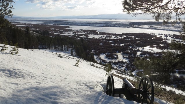 A mountain howitzer cannon sits on a snowy hillside overlooking a wintry valley.