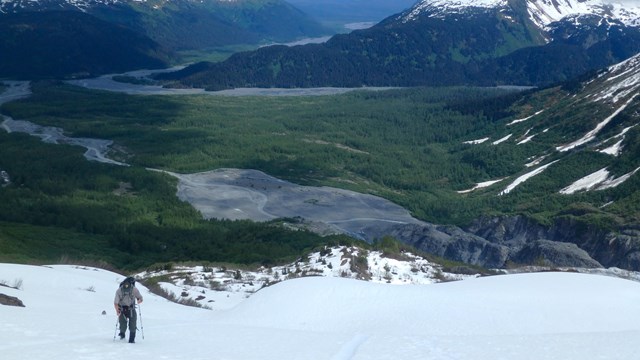 A ranger walks up a snowy slope with valley beyond
